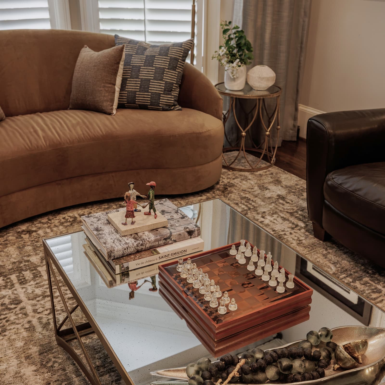 A layered Atlanta living room with a curved caramel sofa, mirrored cocktail table and a chess set — finishing details resolved by Studio Black Oak.